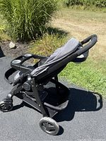 Side view of the gray and black Graco convertible stroller showing the child tray with two cup holders, seat pad, large storage basket underneath, and handlebars.