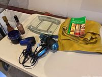 Photo showing two hair dryers, a glass bathroom scale, upholstery material, and instruction book on a white table.