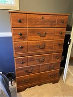 Front view of wood highboy dresser showing 5 drawers with wood and metal handles, light scratches visible.