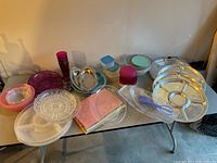Wide view of the table filled with aluminum trays, plastic platters, nesting bowls, containers, and tablecloth.