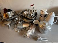 Photo showing assortment of kitchenware including insulated carafes, metal pots, gadgets, and utensils all grouped on a surface, illustrating the variety and condition of the items.