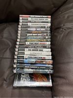 Stack of 19 PlayStation 2 game cases displaying side titles showing game names such as Gran Turismo 3 A-Spec, Medal of Honor, Tiger Woods PGA Tour 06, Grand Theft Auto III, Fight Night Round 3, FIFA Soccer 2003, Hitman 2, among others.