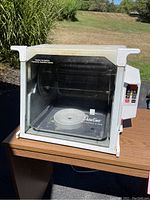 Showtime Set It and Forget It rotisserie, clear glass front with white frame and control panel on side, placed on wooden table outdoors