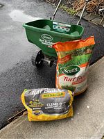 Full lot image showing Scotts EdgeGuard DLX broadcast spreader with two bags of lawn treatment: 40 lb. Turf Builder and partial Weed & Feed.