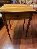 Front view of a small solid pine wood table with drawer and carved tapered legs on hardwood floor.