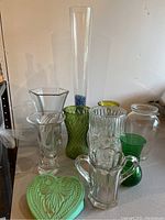 Photo showing a variety of glass vases in clear, green, and yellow colors including a tall clear vase with blue decorative material inside.