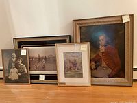 Four framed wall art pieces arranged on floor showing variety of styles and subject matter