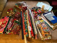 Wide shot showing assorted wrapping paper rolls, ribbons, bows, gift bags, tissue paper, boxes and gift tags.