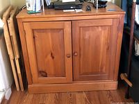 Front view of the wooden cabinet showing two doors with wooden knobs, natural wood finish, and no contents inside.