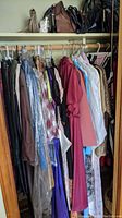 Closet with various women's dresses and slacks hanging on hangers, pocketbooks on shelf above