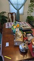 Wood dining table with two leaves attached, smooth polished surface, Queen Anne style curved legs visible. Several objects on top including a silver teapot and flower pot.