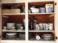 Two cabinet shelves with assorted bone china and porcelain dinnerware including plates, cups, and serving pieces.
