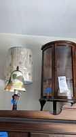 Combined view of small wood and glass display case, reverse painted bell-shaped parlour lamp, and metal base table lamp with wrapped shade