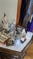 View of assorted figurines, trinket box, greeting cards box, mannequin with jewelry, and surge protector on a marble top wooden table.