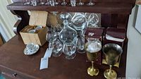 Overview of glassware set including demitasse cups, decanter, brandy glasses, and brass goblets on wooden surface.