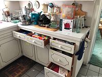 Kitchen countertop and open drawers showing contents of kitchen towels, gadgets, flatware, and utensils.