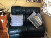 Front view of the green leather La-Z-Boy loveseat with three cushions placed on the seats, showing wear on the leather upholstery.