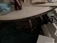 Close-up photo of ornate metal legs and part of marble tabletop edge.