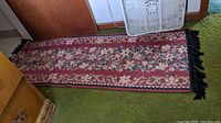 Full view of a floral patterned runner with black fringe, showing overall wear and a red background with pink and green floral motifs.
