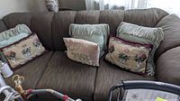 Photo of brown upholstered sofa with multiple decorative pillows including floral and fringed designs.