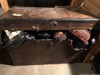 Front view of large vintage steam trunk partly open, showing interior with bags and cushions.