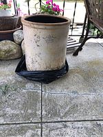 12-gallon stoneware crock pot placed on patio concrete floor surrounded by outdoor furniture and plants.