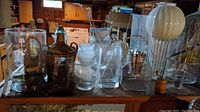 Overview of glass vases, bottles, glass lamp globe, and assorted containers on a table in basement setting