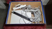 Box containing white Nintendo Wii accessories including power supply, sensor bar, cables, and controller.