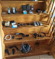Full view of stairs displaying all items arranged across the steps including phones, devices, remotes, headphones, chargers, and accessories.