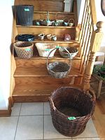 Seventeen assorted baskets arranged on wooden stairs showing variety in size and shape. Includes large dark brown Demijohn basket at bottom step.
