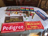 Overview photo showing all beer tap heads with various logos and six colorful bar towels on a white fabric surface.