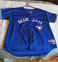 Front view of blue Blue Jays short-sleeved shirt laid flat showing button closure, logo, and text.