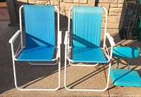 Photo showing two matching blue folding lawn chairs with white metal frames side by side with a vintage blue stadium seat nearby.