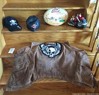 Harley Davidson suede vest alongside caps, metal plaque and motorcycle bank on wooden steps.