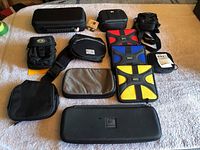 Top-down view showing eleven assorted cases arranged on a surface, including black, gray, and brightly colored padded media cases of various sizes and styles.