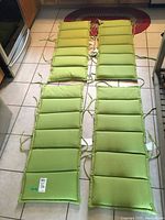Set of four green fabric chaise lounge cushions laid out on the floor, showing full length and tie straps on sides.