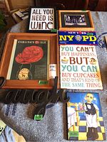 Photo showing seven assorted decorative wall signs with themes of beer, wine, cupcakes, NYC, and a cartoon waiter. Several framed pieces include a Carling's Ale advertisement and black and white bar photo.