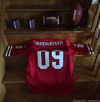 Spalding leather football, football-shaped musical snack dispenser, football-themed drink sleeves, and Budweiser 09 shirt laid out on wooden stair steps