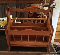 Front view showing the scalloped edging and vertical rods inside the wooden magazine rack with handle.