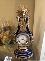 Front view of lyre-shaped porcelain clock showing dial, sunburst motif, and gilt decoration