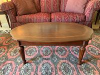Front view of wooden coffee table showing carved legs and wood grain top surface placed in front of a patterned fabric sofa.