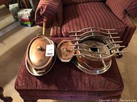 Overview of copper cookware set showing three main items: oval pot, frying pan, and chafing dish on armchair