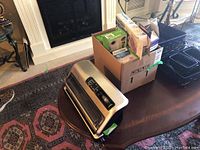 Full photo of the FoodSaver vacuum sealer machine on a wooden table with a cardboard box containing vacuum sealer bags and rolls nearby.