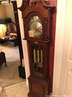 Full front view of the grandfather clock showing woodwork and clock face with weights and pendulum inside glass door.