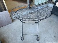 Side view of the ornate metal tray and stand on patio concrete floor near sliding door, shows rust and detailed scrollwork.