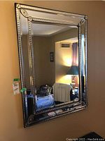 Frontal view of the rectangular mirrored wall mirror showing the framed beveled mirror border with leaf corner decorations.