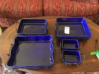 Front perspective of five blue ceramic oven ware dishes of varying size on wire stands with wicker accents.
