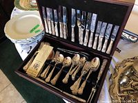 Wooden case open showing top row of plated knives and bottom tray with forks, spoons, certificate
