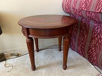 Front angle view of round wooden side table next to a patterned sofa, showing carved legs and top detail
