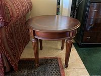 Side view of round wooden side table showing profile, fluted legs, and carved details.